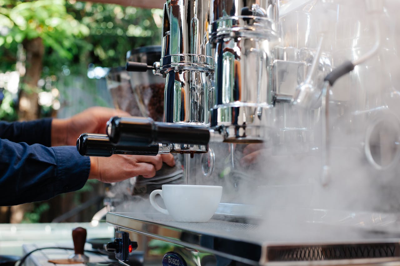 Unrecognizable professional barista working on coffee machine with steam while making coffee on street against blurred background during work process